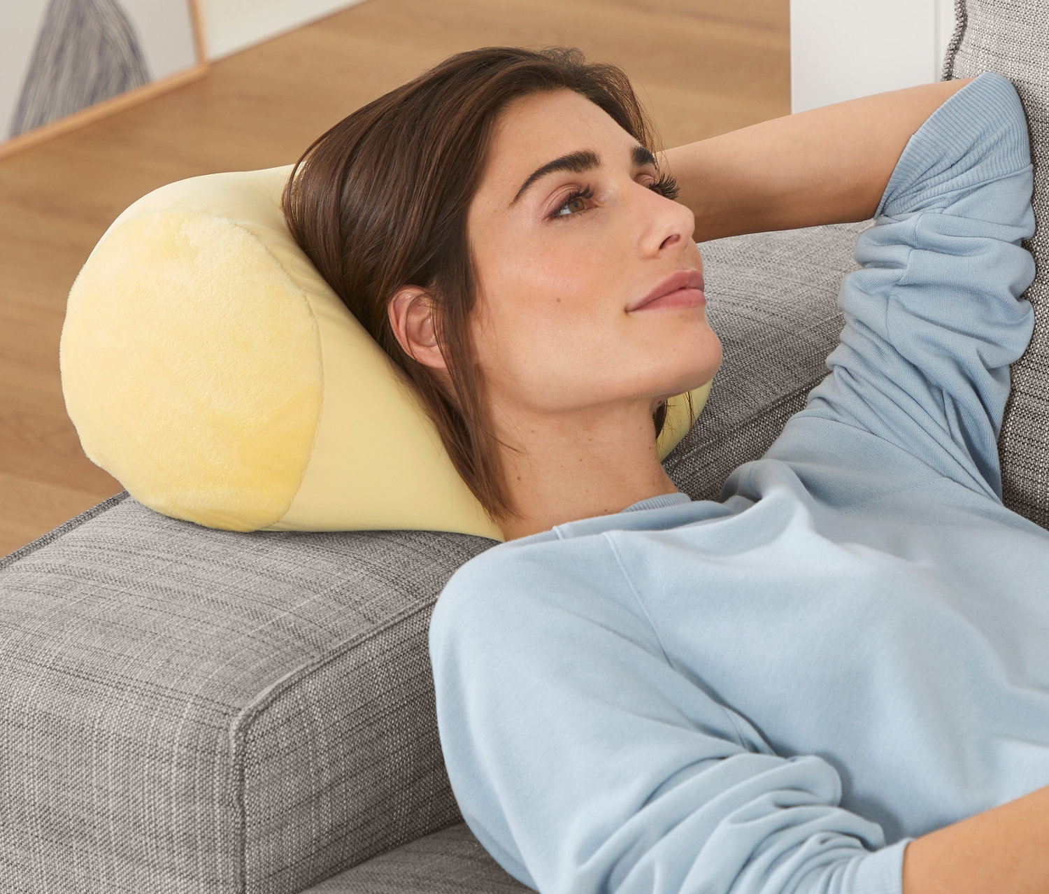 Une femme est allongée sur un canapé gris avec un coussin de relaxation.