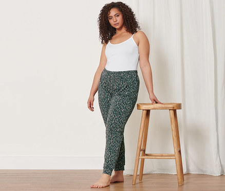 Femme en caraco et pantalon relax appuyée sur un tabouret en bois. Elle porte aussi 2 caracos.
