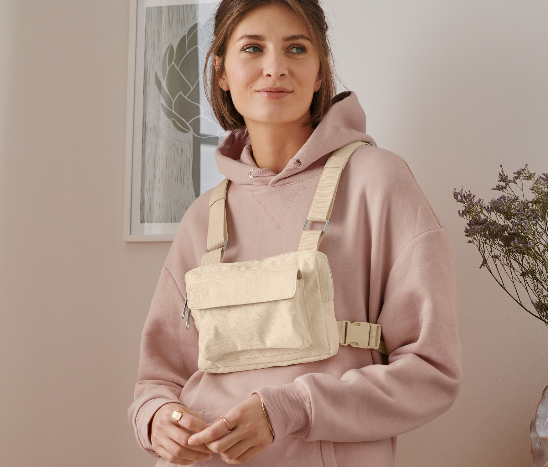 Femme portant un sac à bandoulière polyvalent beige et un sweat à capuche rose.