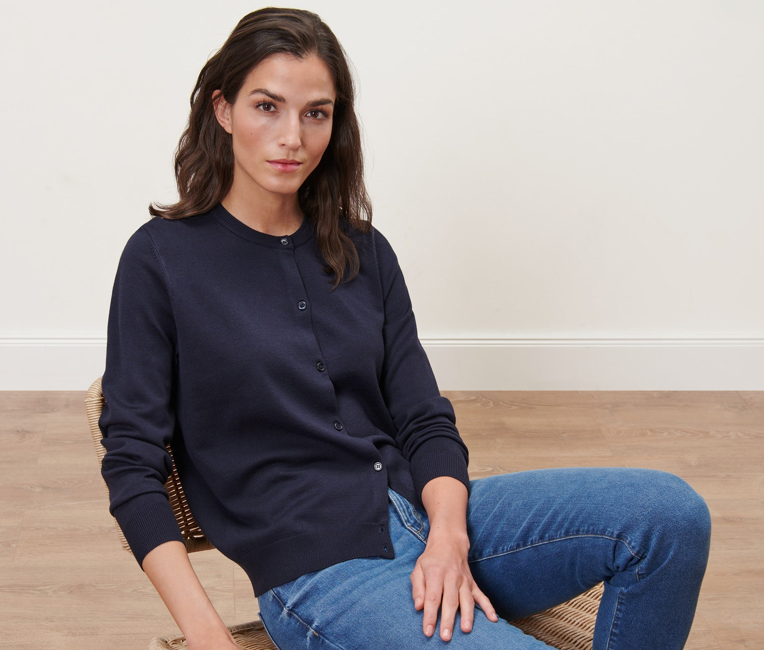 Femme assise sur une chaise portant un cardigan bleu marine en maille fine.