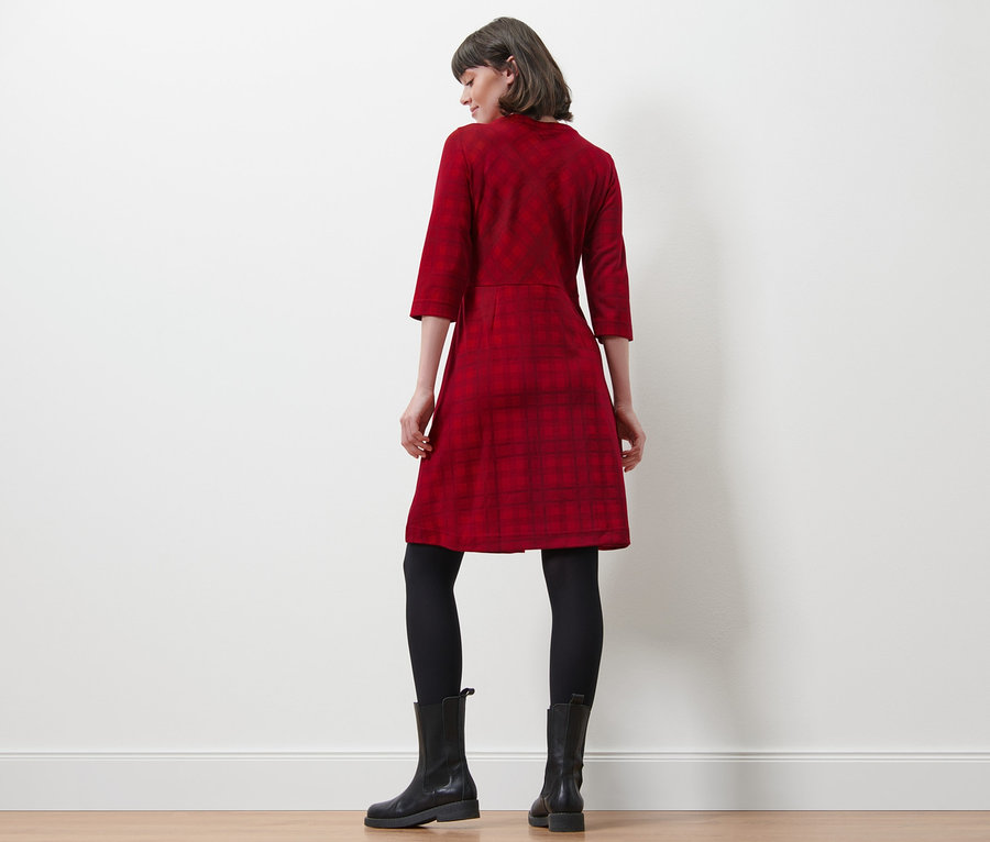 Une femme, vue de dos, porte une robe en jacquard à carreaux, des leggings noirs et des bottes noires.