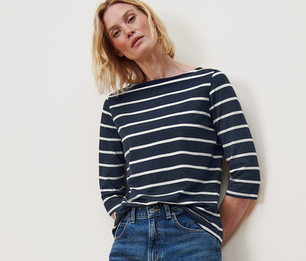 Femme posant en t-shirt manches 3/4 à rayures, jean bleu et baskets blanches.