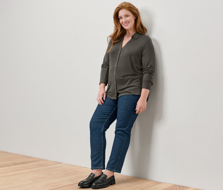 Une femme appuyée contre un mur porte une blouse avec patte de boutonnage et un jean droit – Fit «	Juna	».