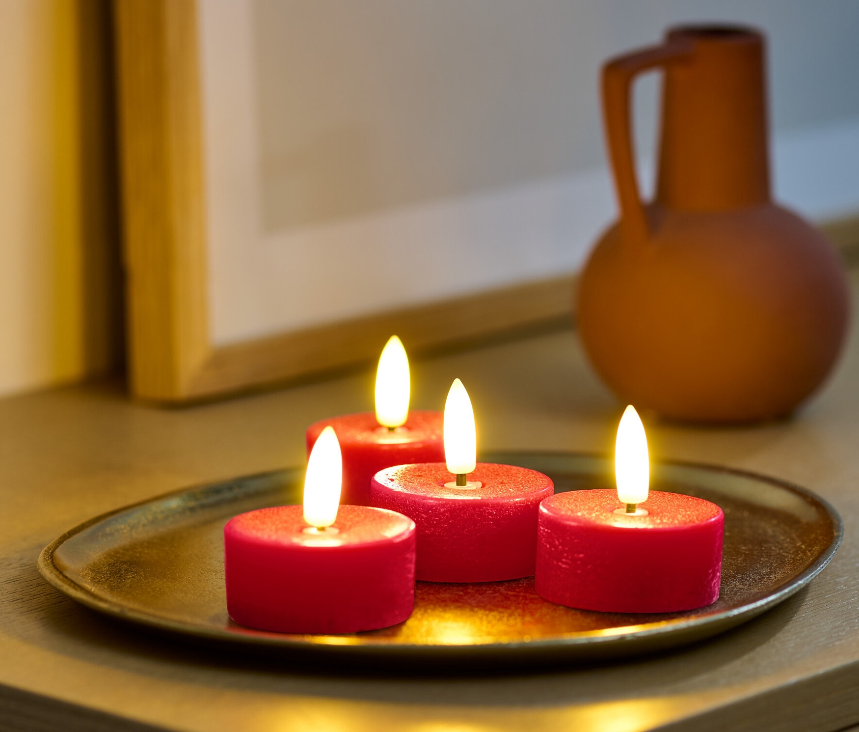 Quatre bougies chauffe-plat rouges à LED en cire véritable sur un plateau doré sur une armoire.