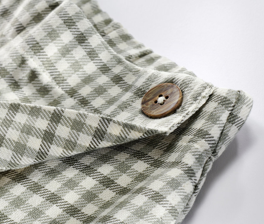Gros plan sur une jupe-culotte pour enfant avec un bouton marron et un motif à carreaux.