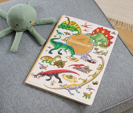 Sur un tabouret gris sont posés un livre « Dinosaurier Wimmelbuch » et une peluche de pieuvre verte.