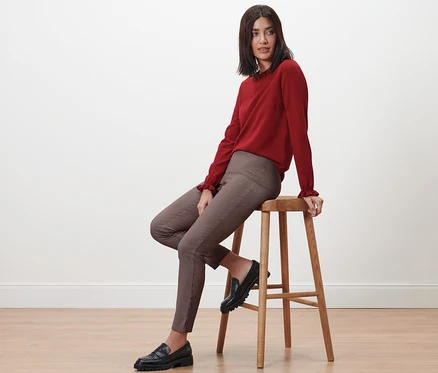 Une femme assise sur un tabouret porte un pantalon stretch à carreaux.