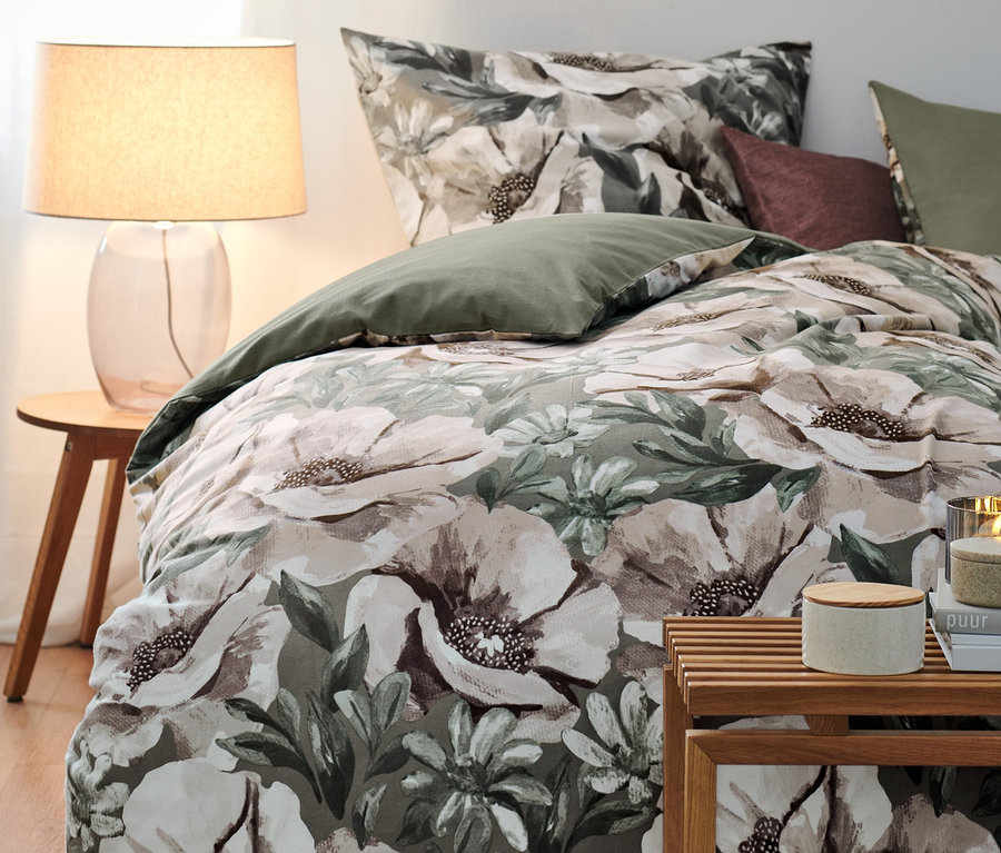 Une parure de lit en molleton à motif floral est posée sur un lit à côté d'une lampe et d'une table.