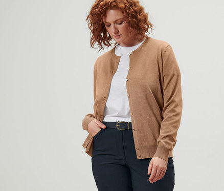 Une femme porte un cardigan en maille fine, une ceinture en cuir et un pantalon en bengaline bleu foncé.