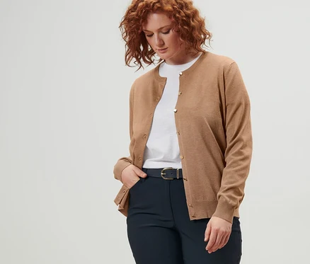 Une femme porte un cardigan en maille fine, une ceinture en cuir et un pantalon en bengaline bleu foncé.