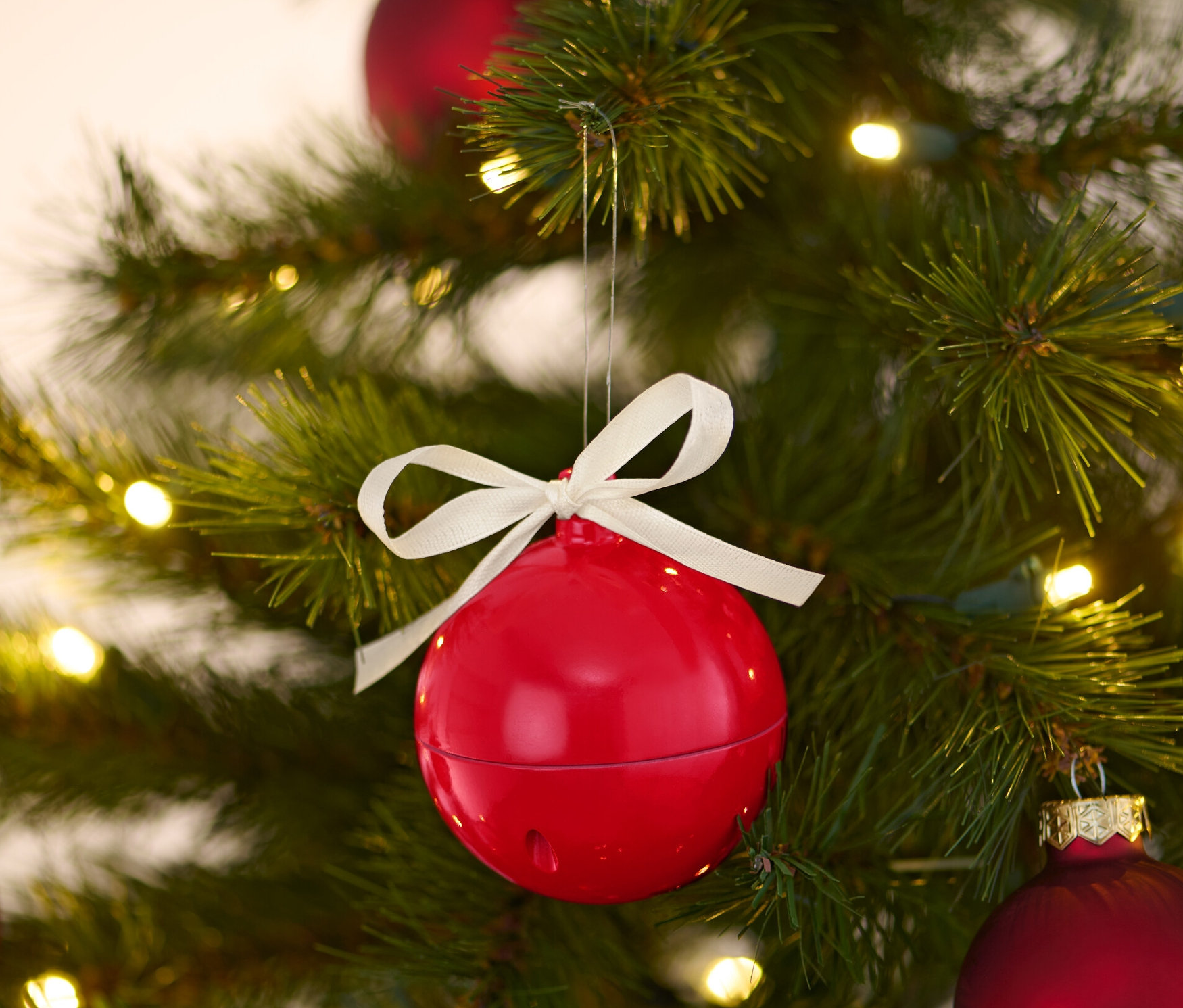 Une boule de Noël musicale rouge est suspendue à un arbre de Noël avec d'autres boules rouges et des lumières.