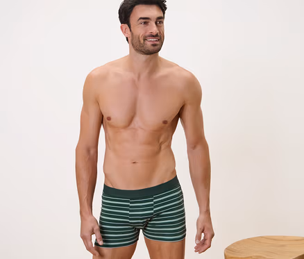 Un homme pose en 4 Boxers, gris, à côté d'un tabouret en bois.