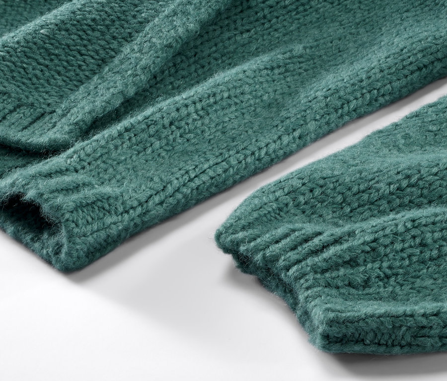 Gros plan sur un cardigan ouvert en grosse maille vert.