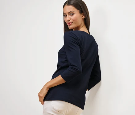 Une femme regarde par-dessus son épaule et porte un t-shirt bleu marine à manches 3/4.