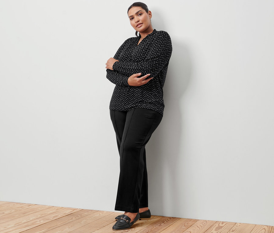 Une femme pose en pantalon en jersey noir avec nervure et un t-shirt manches longues avec encolure en V et imprimé intégral.