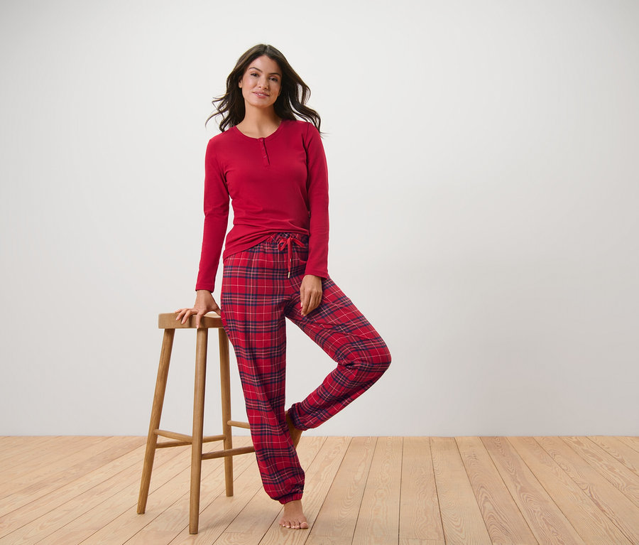 Femme posant en pyjama de flanelle rouge à carreaux, une main sur un tabouret en bois.