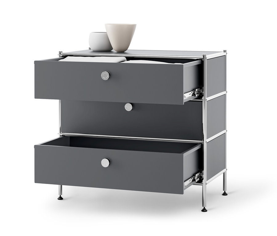 Une commode en métal grise « CN3 » avec trois tiroirs dont deux sont ouverts. Deux vases sont posés sur la commode.