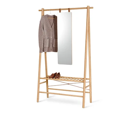 Un cardigan marron clair est suspendu à un cintre à côté d'un miroir sur un support en bois avec des chaussures sur l'étagère inférieure.