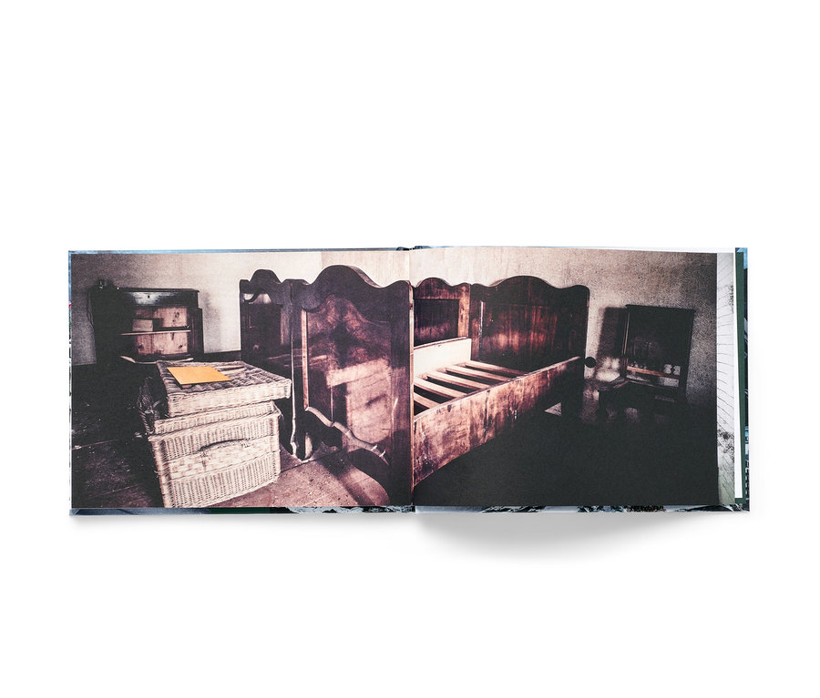 Un livre ouvert montre une vieille chambre avec un lit en bois, une commode et des paniers en osier.