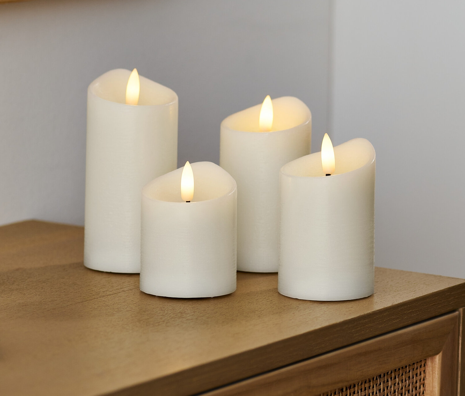 Quatre bougies à LED en cire véritable crème sont posées sur une commode en bois.