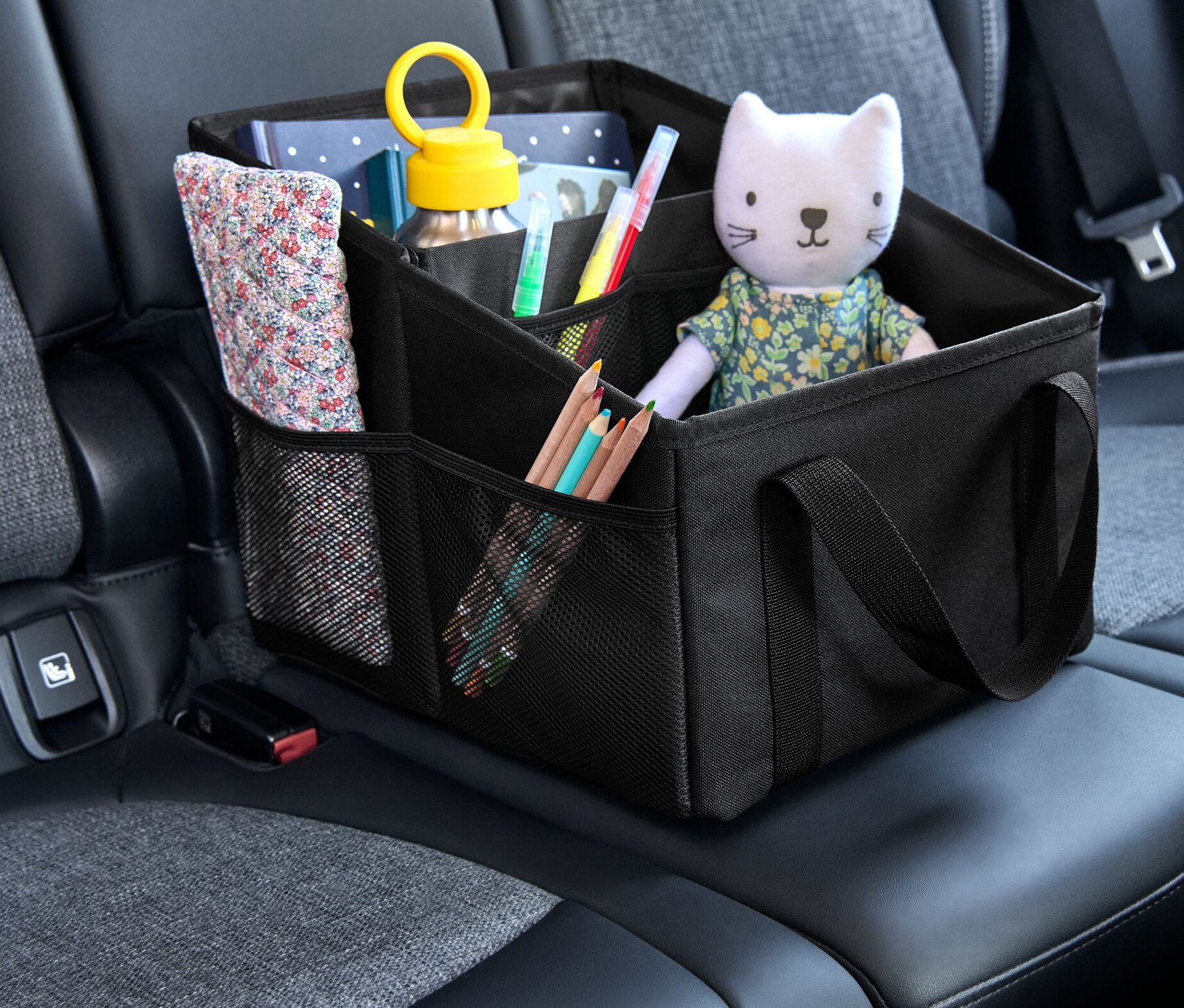 Un rangement pour siège de voiture noir est placé sur le siège auto. Des crayons de couleur, une boisson, un livre et un chat en peluche se trouvent dans le rangement.