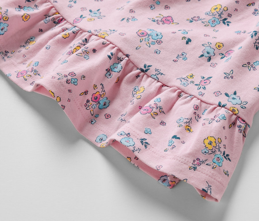 Gros plan sur une robe en jersey rose pour bébé avec un imprimé floral et des volants.
