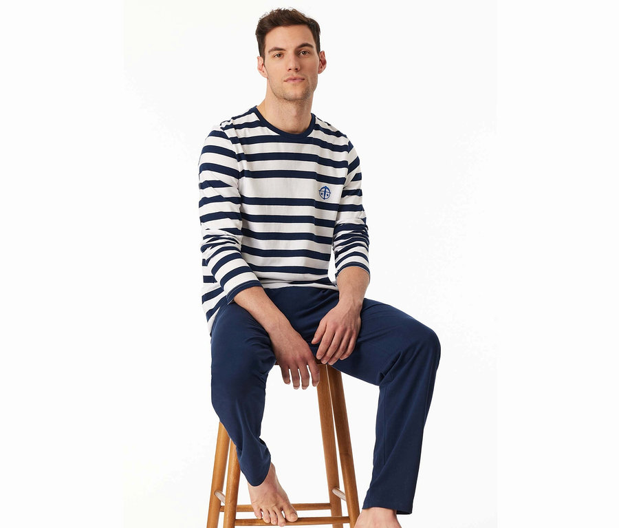 Un homme est assis sur un tabouret en bois, portant un t-shirt rayé à manches longues et un pantalon bleu.