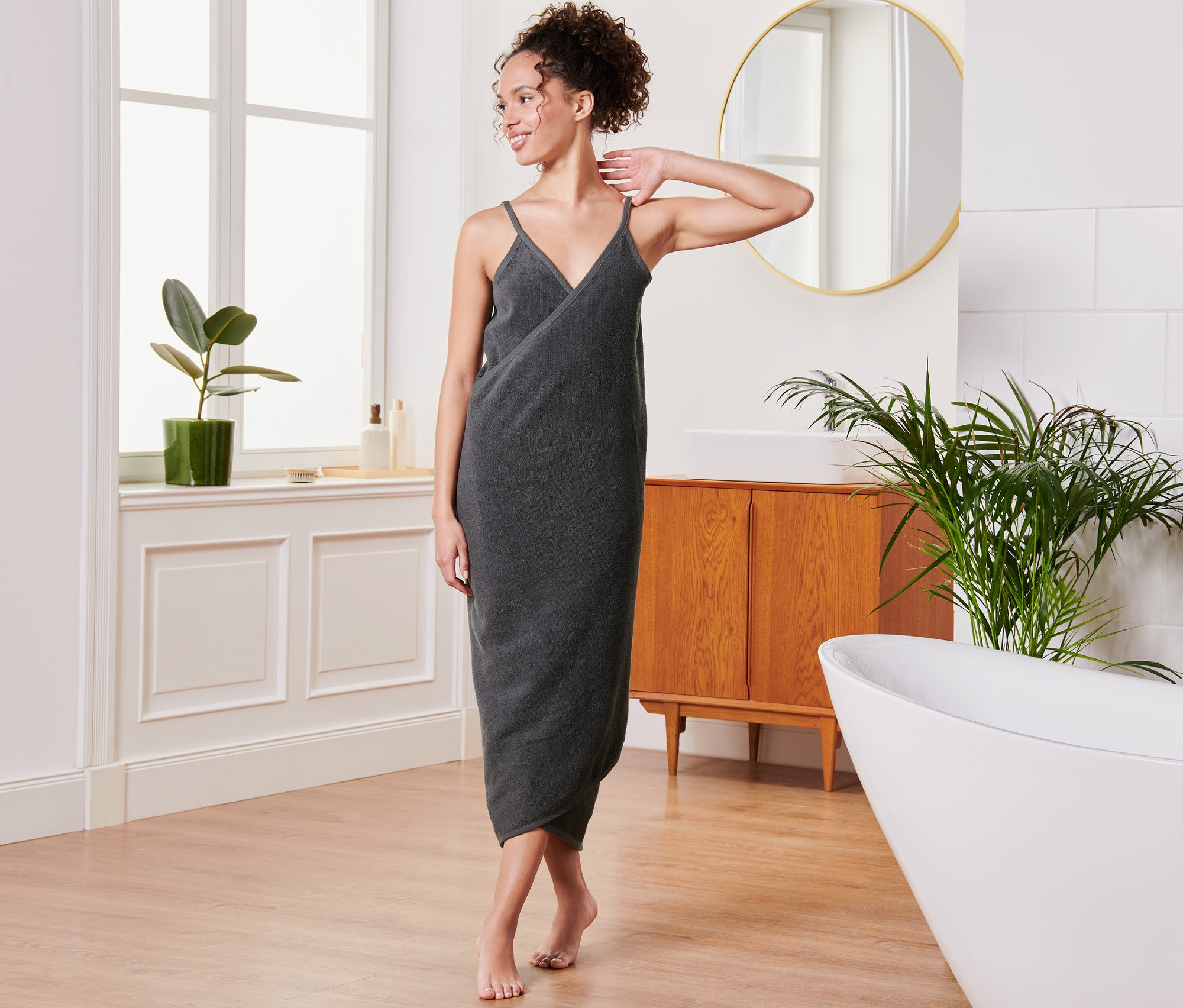 Une femme pose dans une salle de bain dans une robe de bain anthracite.