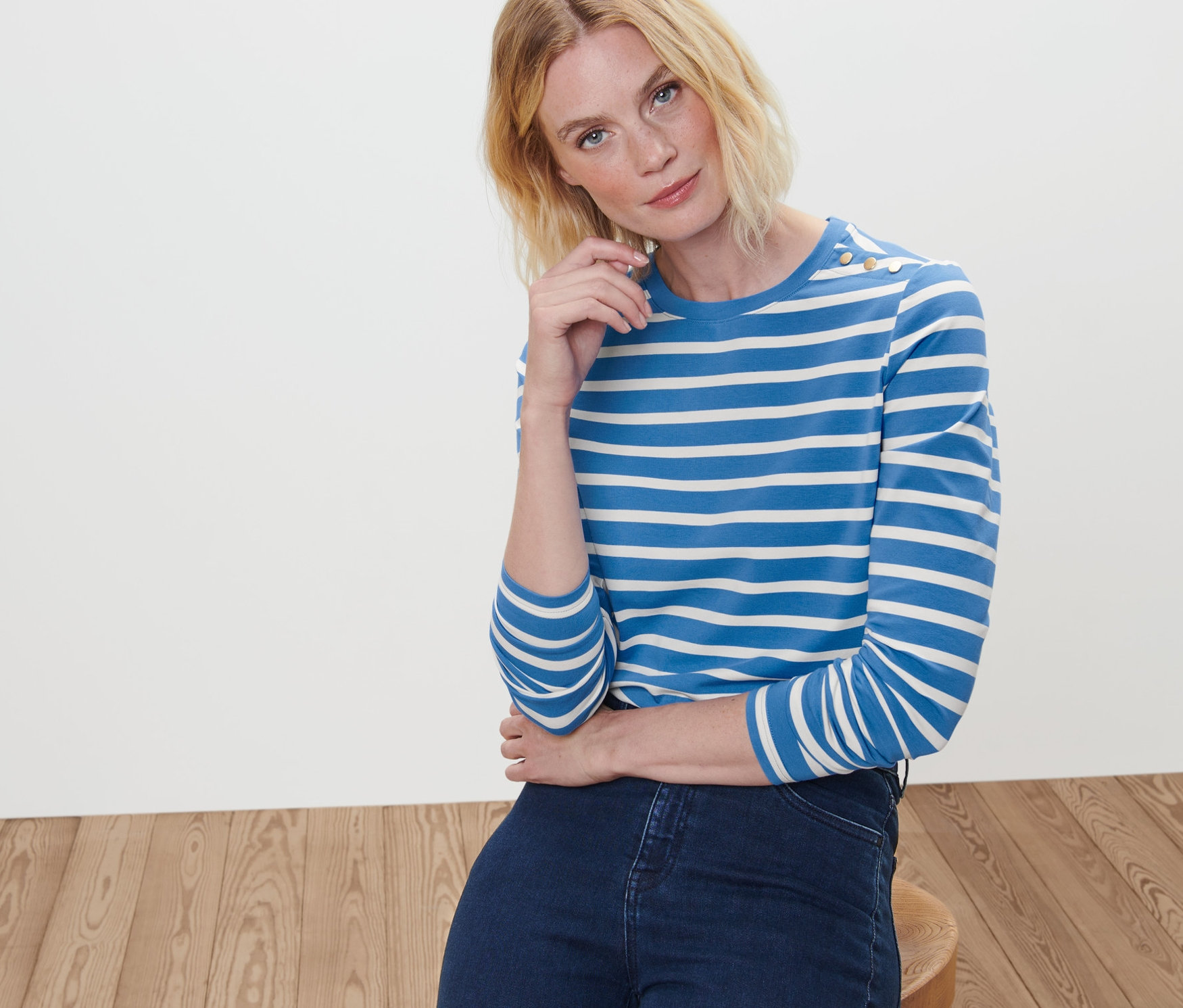 Une femme blonde est assise et porte un T-shirt manches longues à rayures et un jean.