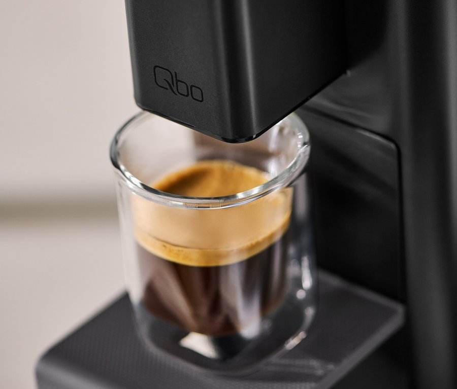 Gros plan d'une machine à café Qbo ICONIC Dark Chrome avec une tasse de café.