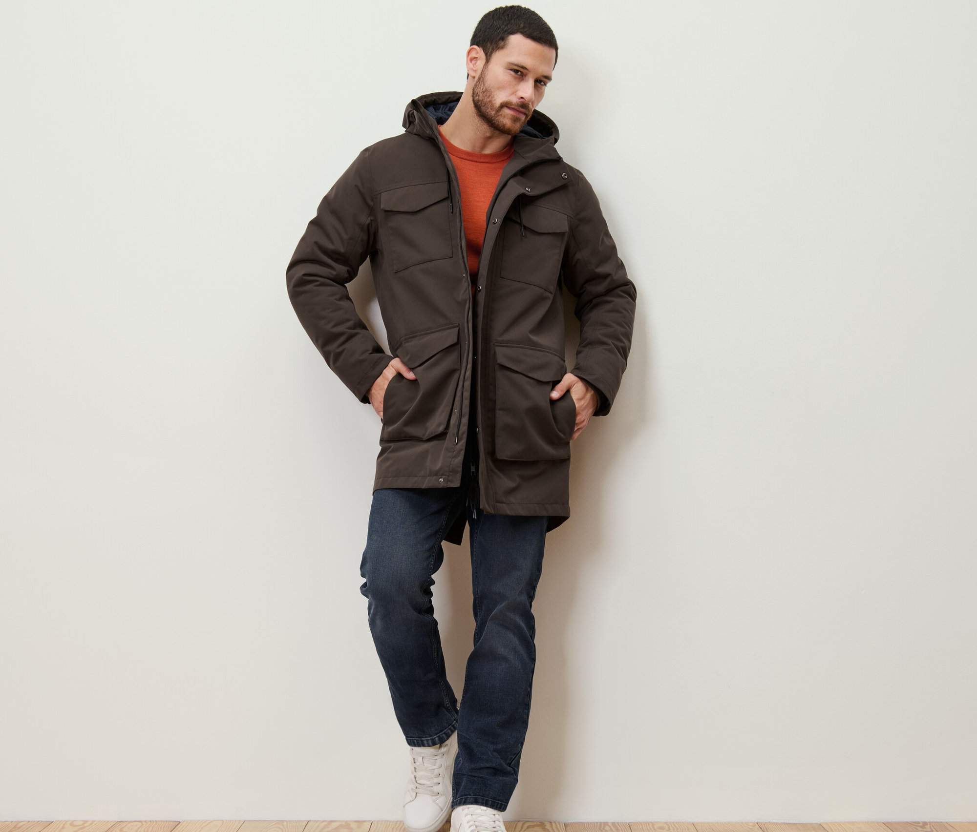 Un homme appuyé contre un mur portant une parka.