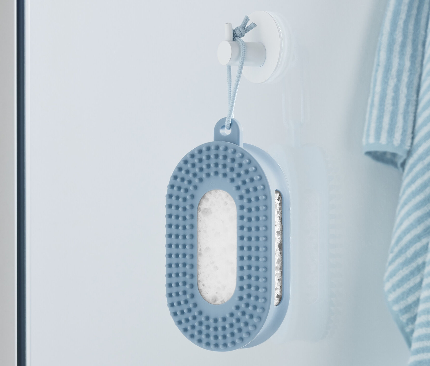 Une éponge de douche bleue est accrochée au mur à côté d'une serviette rayée.