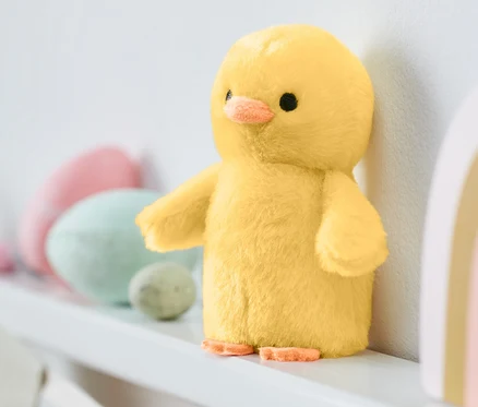 Un poussin jaune avec son se tient sur une étagère blanche.