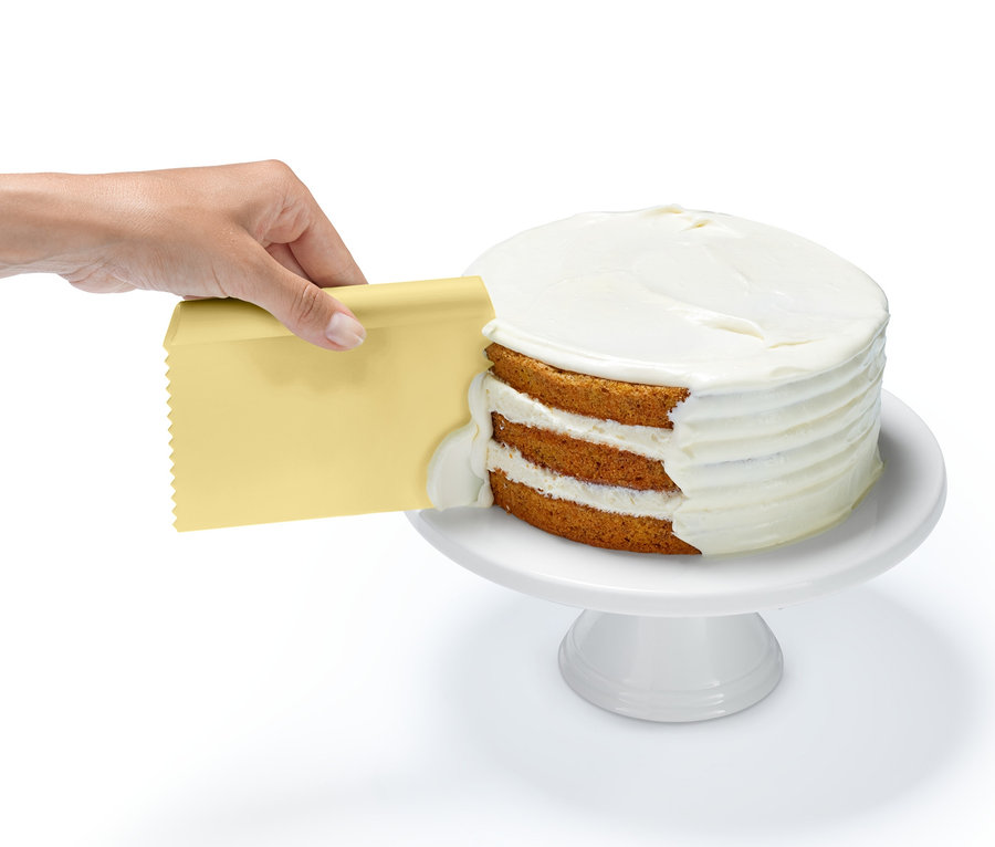Une main étale du glaçage sur un gâteau à l'aide d'un grattoir jaune du kit d'accessoires professionnels de pâtisserie.