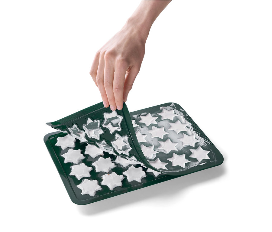Une main retire un moule en silicone vert en forme d'étoile d'une plaque à pâtisserie avec des étoiles blanches.