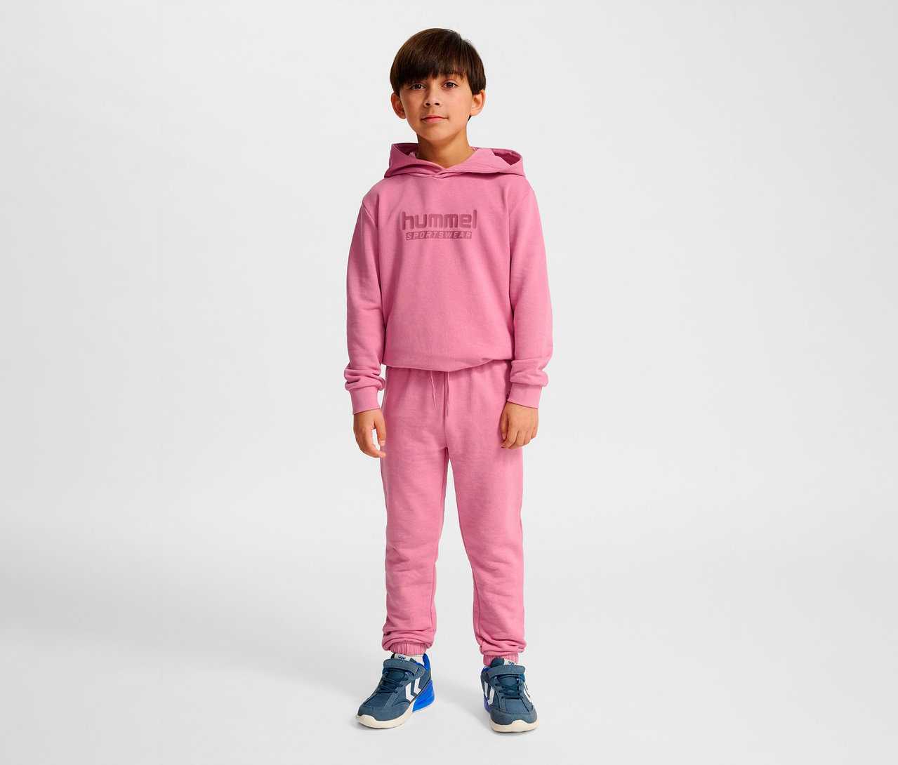 Un garçon debout portant un ensemble rose HUMMEL HMLJR Base Regular Pants.