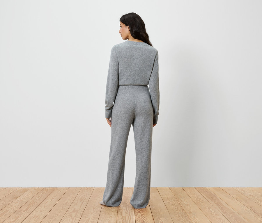 Une femme, vue de dos, porte un haut en tricot gris à manches longues et un pantalon large.
