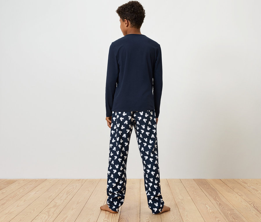 Un garçon se tient dos à la caméra, portant un haut de pyjama bleu à manches longues et un pantalon de pyjama imprimé avec des ours en peluche blancs.