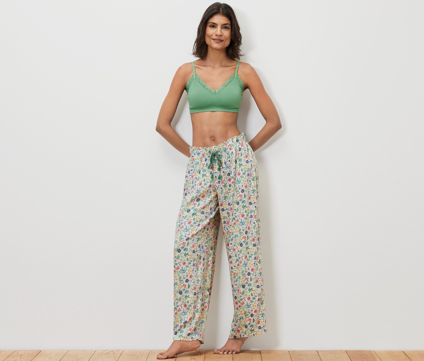 Femme posant en bralette en dentelle verte et pantalon relax à motif floral.