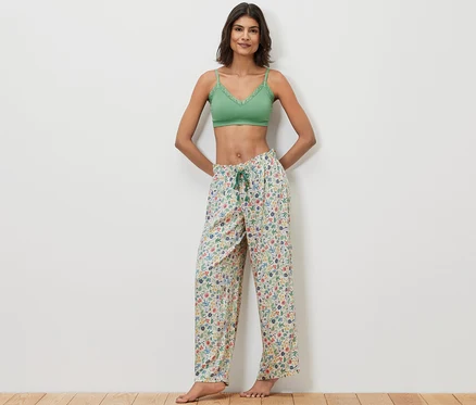 Femme posant en bralette en dentelle verte et pantalon relax à motif floral.