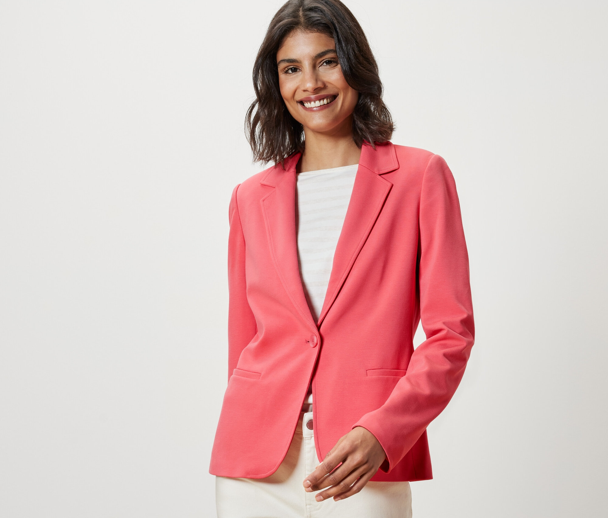 Femme souriante portant un blazer en jersey corail.