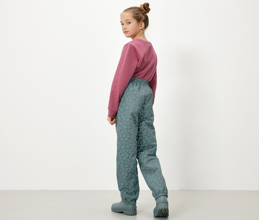 Fillette portant un pull et un pantalon de pluie pour enfants avec des éléments réfléchissants, vue de dos.