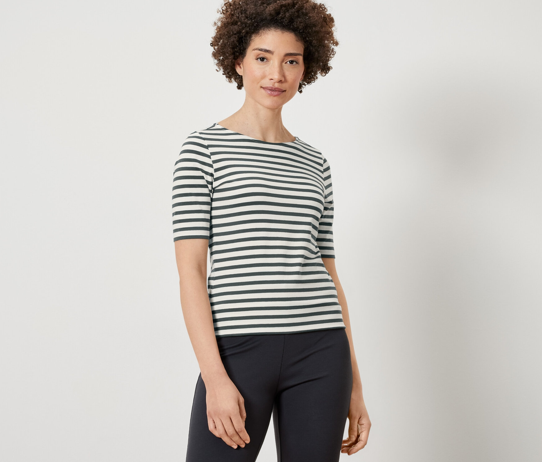 Une femme porte un t-shirt à rayures vertes à manches et un pantalon noir.