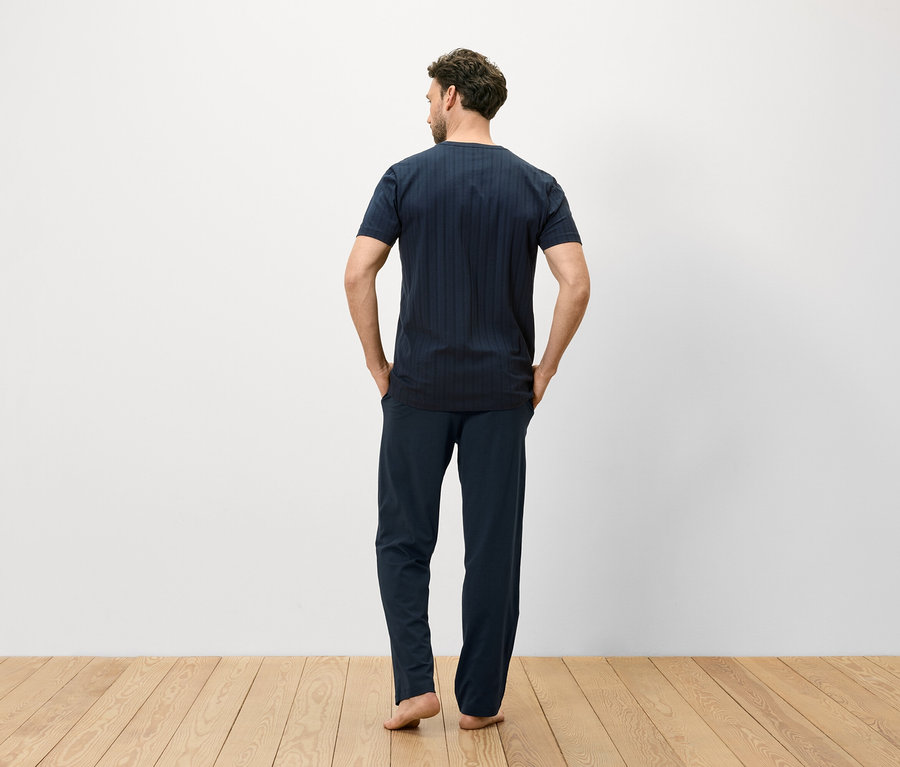 Homme vu de dos portant un t-shirt rayé bleu et un pantalon sur un plancher en bois.