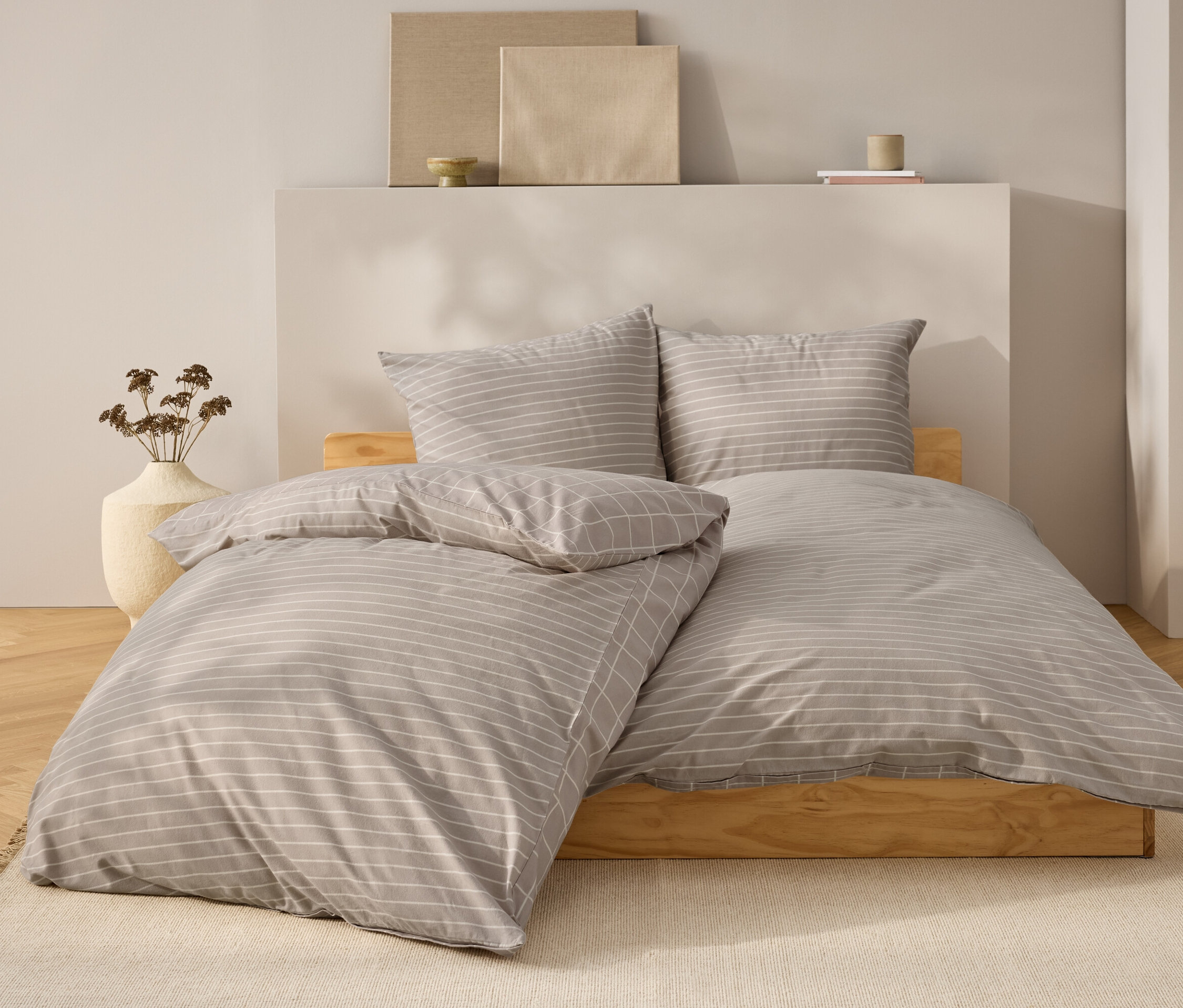 Linge de lit à rayures grises et blanches sur un lit en bois naturel.