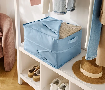 Boîte de rangement en tissu bleu clair avec couvercle sur une étagère blanche à côté de chaussures et d'un chapeau.