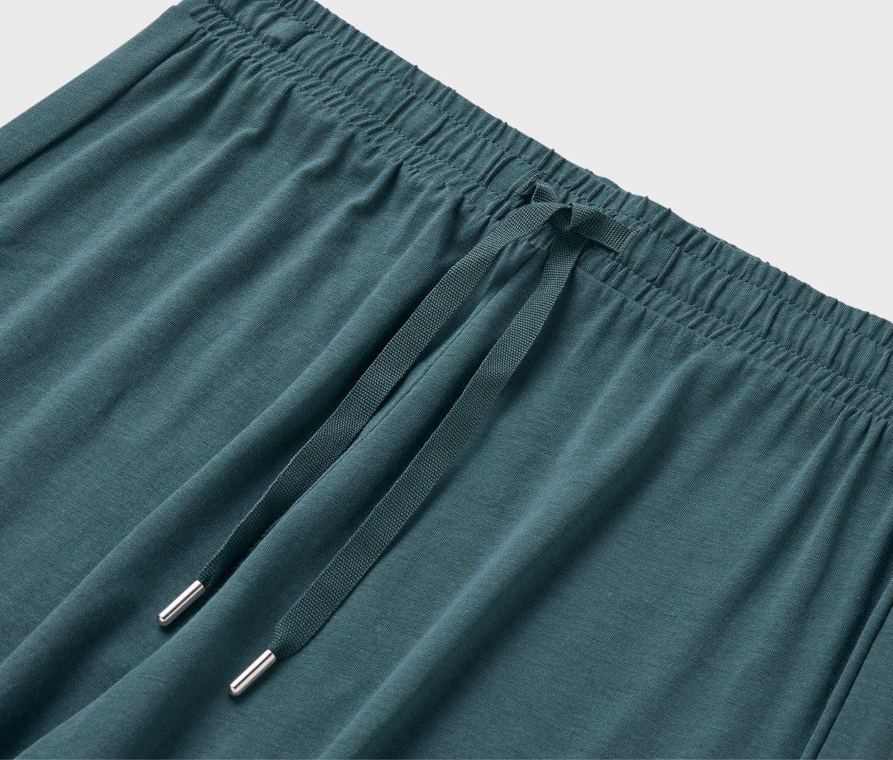 Gros plan sur la taille élastique et le cordon de serrage d'un pantalon de survêtement bleu-vert.