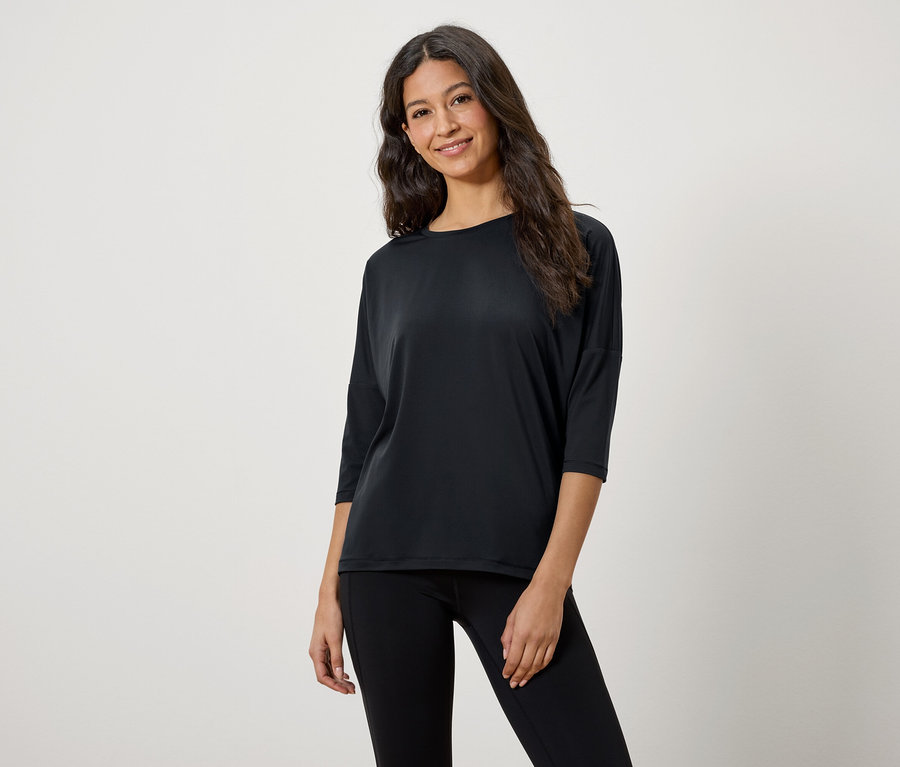 Une femme aux cheveux bruns pose dans un t-shirt noir à manches trois-quarts et un legging noir.