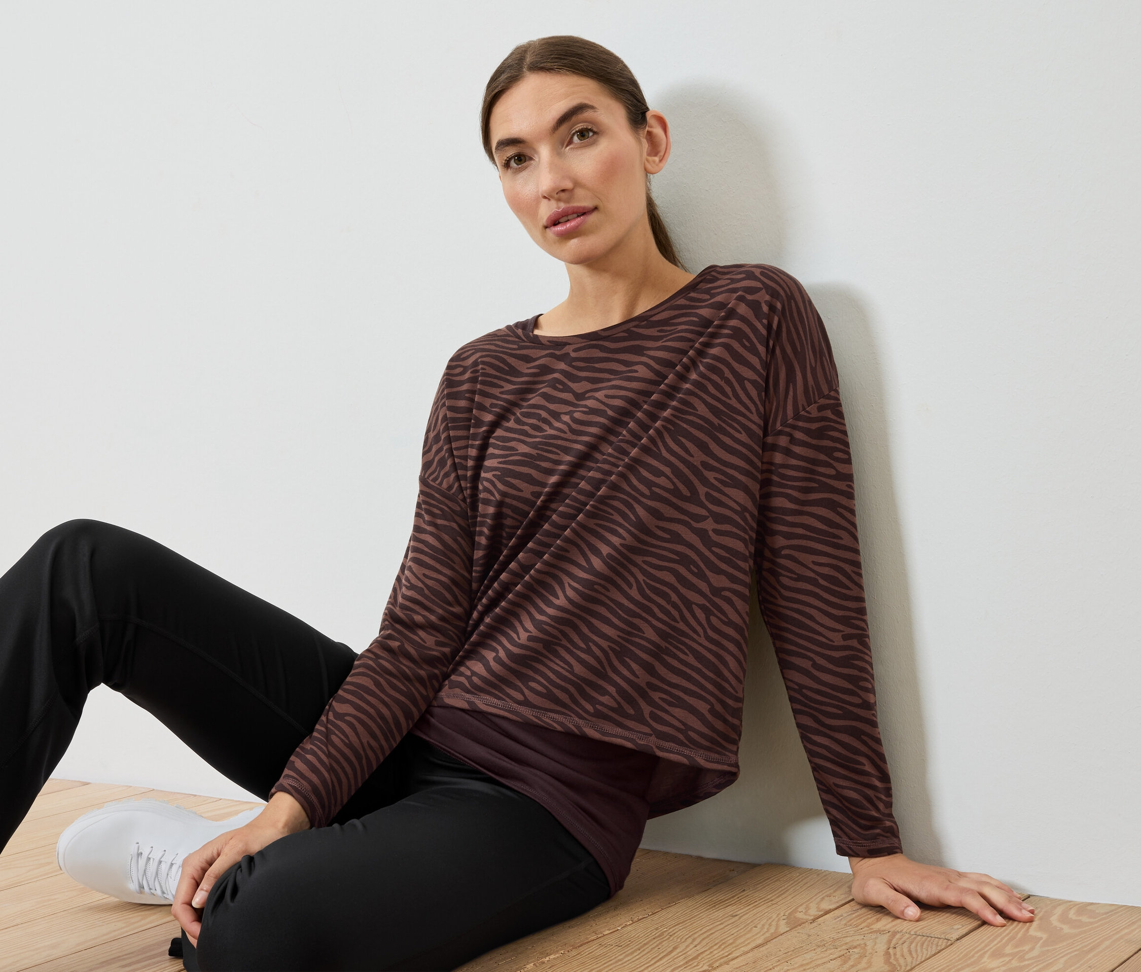 Une femme est assise sur le sol et porte un haut zébré marron et noir et un pantalon noir.