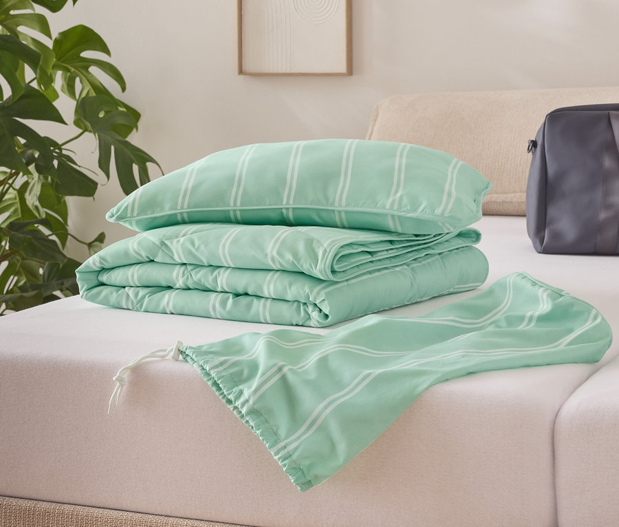 Sur un lit sont posés une couette vert clair pliée à rayures blanches, un oreiller et un sac.